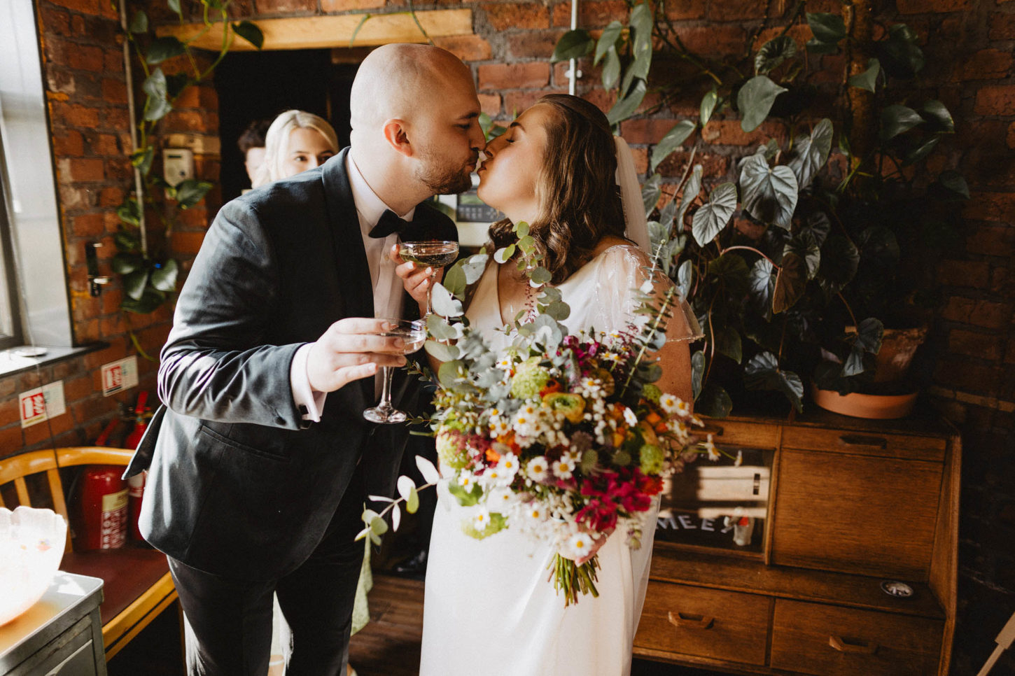 Couple kissing at wedding with champagne and bouquet.